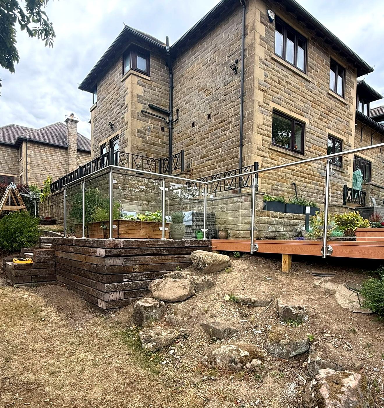 Stainless steel and glass balustrade to a raised patio on a sleeper wall at a stone house, Totley, Sheffield